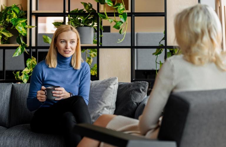 A woman sitting with a cup of coffee while talking to another woman in the Gdansk office in Poland. 
